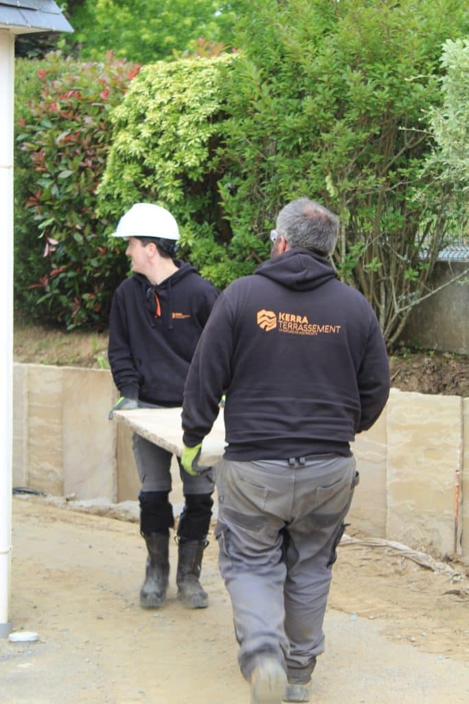 2 techniciens portent une dalle pour aménager un jardin Kerra Terrassement